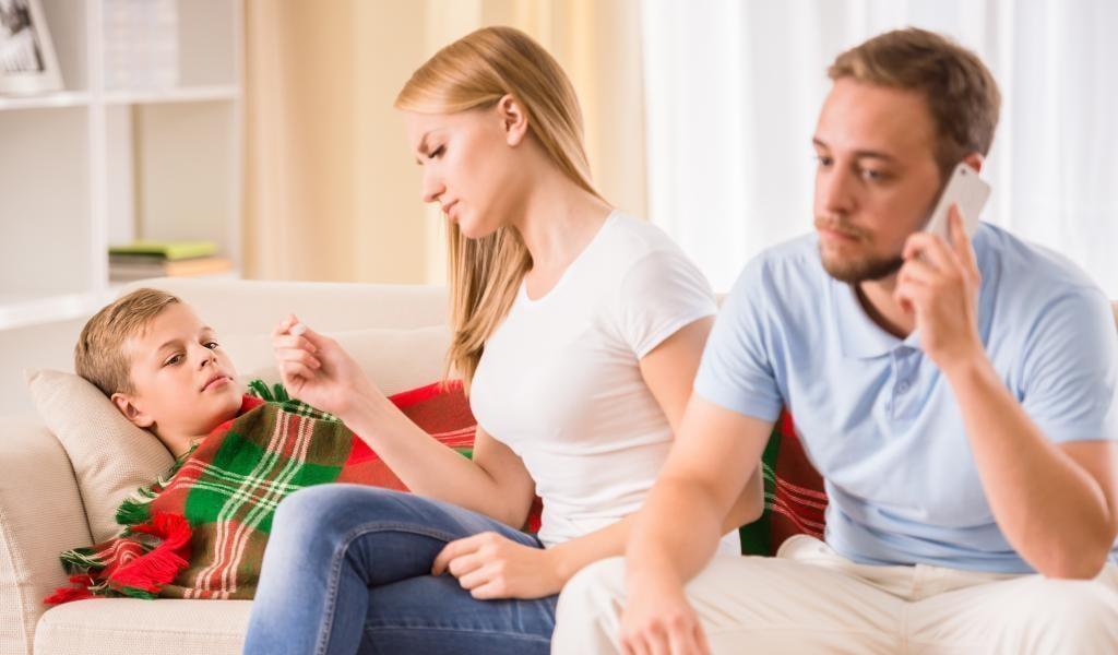 Parents phoning for medical advice for a sick boy lying on a lounge